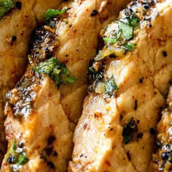 Close-up of sliced grilled chicken breast, garnished with chopped herbs, showcasing a juicy, seasoned texture.