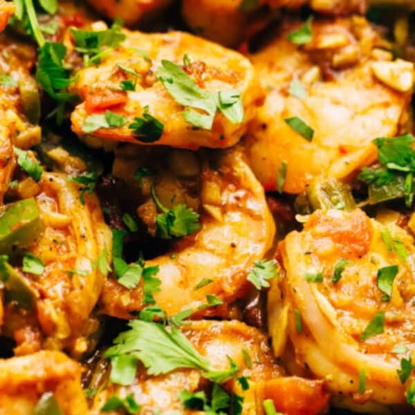 A close-up of succulent shrimp cooked in a savory sauce, garnished with fresh cilantro and mixed with diced vegetables.