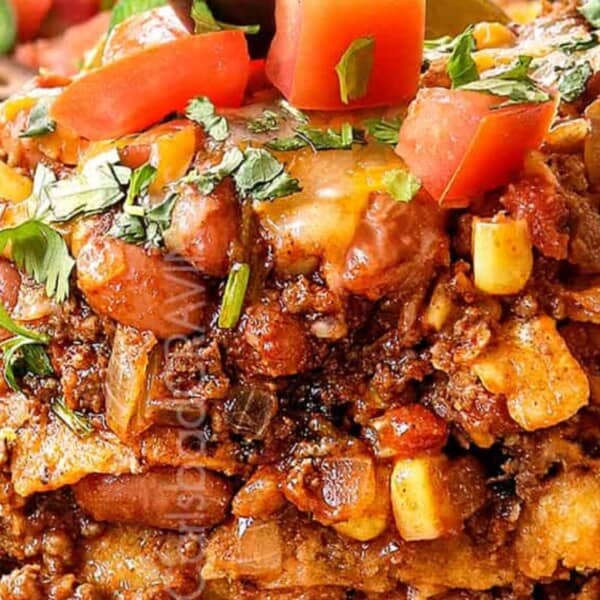 A hearty layered casserole topped with tomatoes and cilantro, surrounded by fresh green peppers, olives, and diced tomatoes.