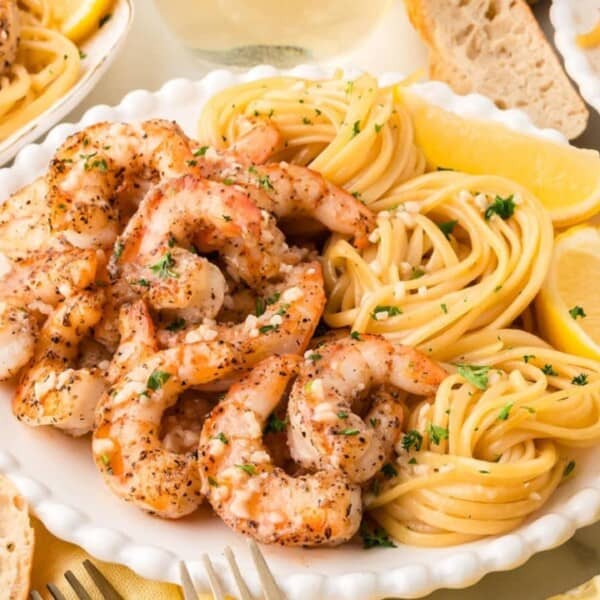 The image features a plate of spaghetti with shrimp, garnished with lemon wedges and parsley. There are also slices of bread next to the plate. Additional similar plates can be seen partially in the background.