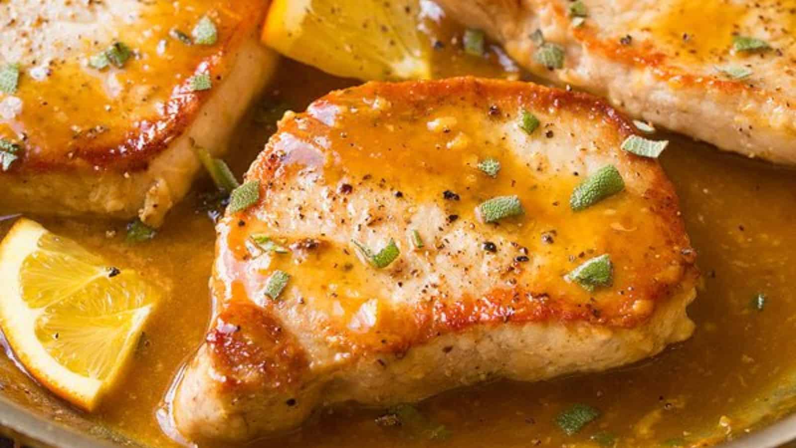 Juicy pork chops in a rich, citrusy sauce, garnished with herbs and served with lemon wedges.