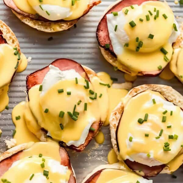 English muffins with leftover ham, poached eggs, hollandaise sauce, and chopped chives on a baking sheet.