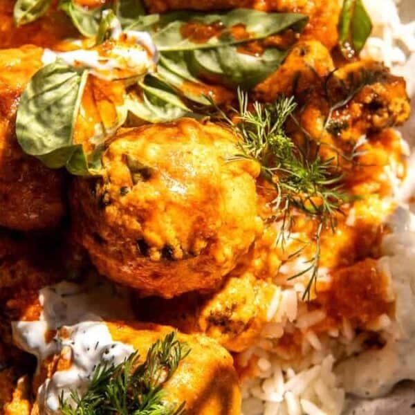 A plate of rice topped with saucy meatballs, garnished with fresh herbs and a dollop of creamy sauce.