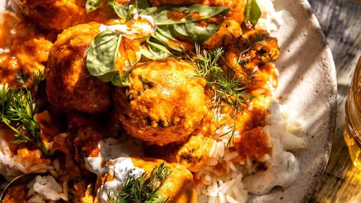 A plate of rice topped with saucy meatballs, garnished with fresh herbs and a dollop of creamy sauce.