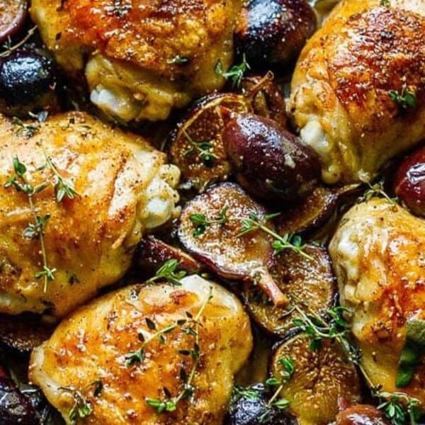 Golden-brown chicken thighs in a skillet with halved figs, onions, and fresh thyme sprigs.