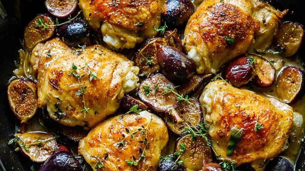 Golden-brown chicken thighs in a skillet with halved figs, onions, and fresh thyme sprigs.
