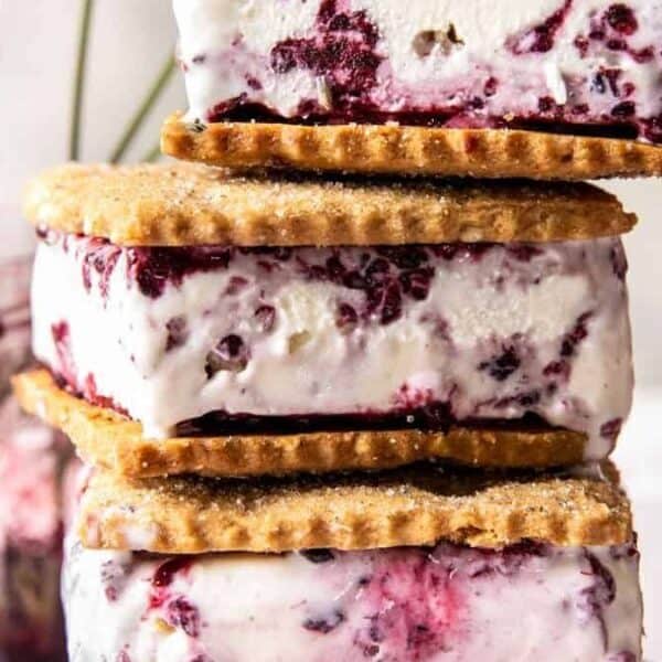 Three rectangular ice cream sandwiches are stacked in the foreground. Each sandwich has a berry-swirl ice cream filling between two graham crackers. Additional sandwiches appear softly blurred in the background.