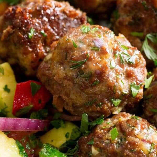 Close-up of meatballs with herbs, next to a salad with diced cucumbers, tomatoes, red onions, and avocados.