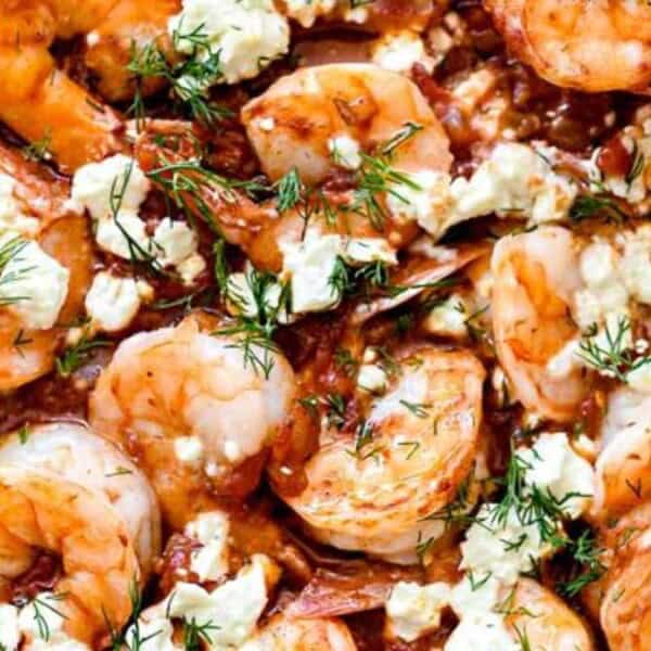 Pan of cooked shrimp in tomato sauce, garnished with crumbled feta cheese and fresh dill.
