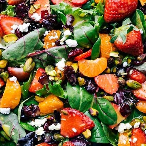 A mixed green salad topped with strawberries, mandarin orange slices, dried cranberries, pistachios, and crumbled cheese.