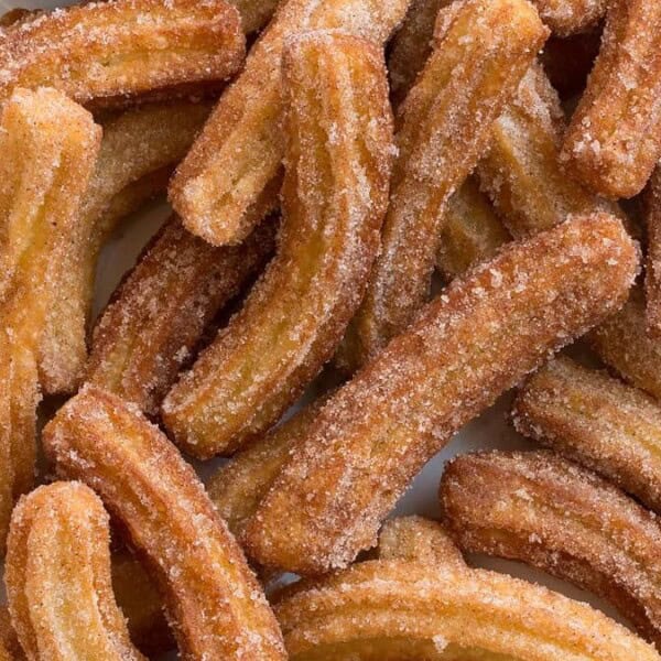 A tray with freshly baked churros, coated with sugar and cinnamon, arranged haphazardly.