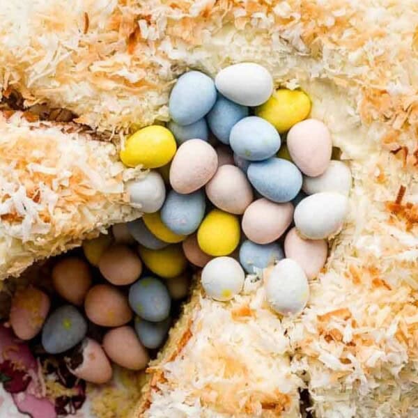 A coconut-covered bundt cake filled with pastel-colored candy eggs sits on a pink floral plate.