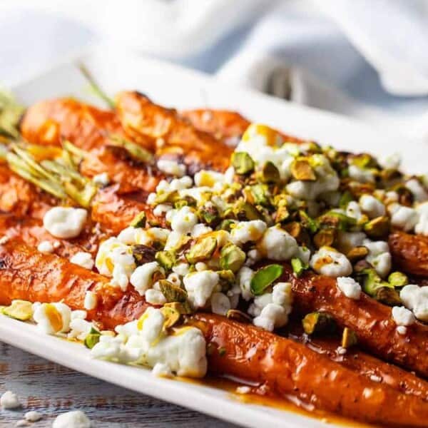 Roasted whole carrots topped with crumbled cheese and chopped pistachios on a rectangular white plate.
