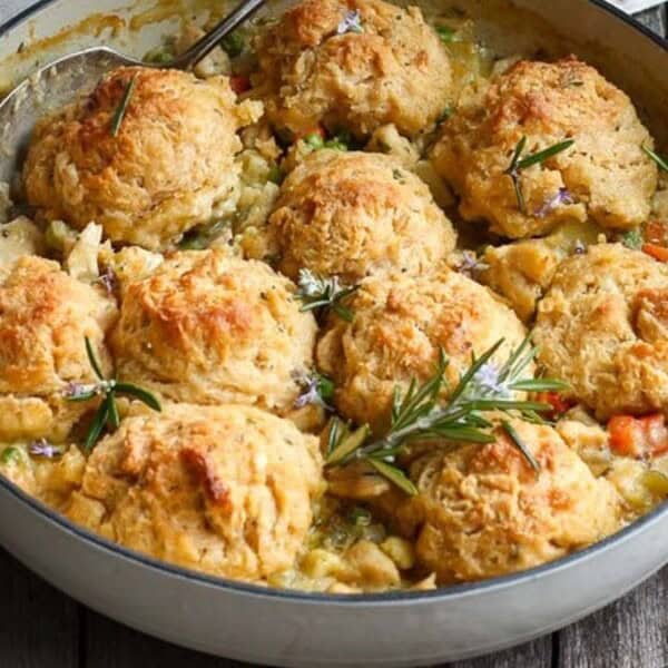 A casserole dish with chicken, vegetables in sauce, and golden-brown biscuit dumplings sits on a wooden table.