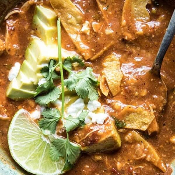 Bowl of tortilla soup with avocado slices, cilantro, crumbled cheese, a lime wedge on top, and a spoon in the soup.