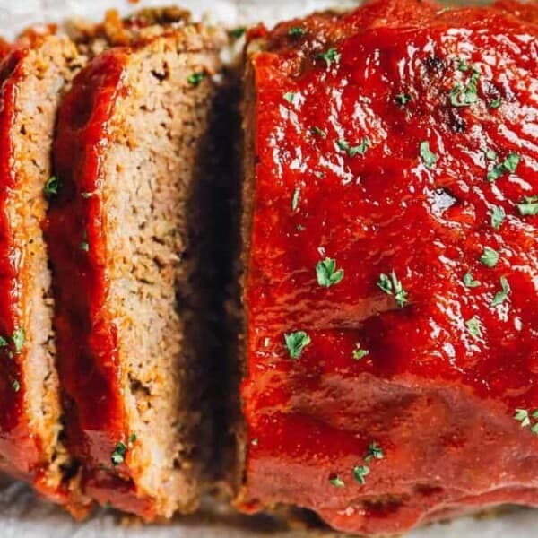 Sliced meatloaf with tomato sauce and chopped herbs on top, arranged on parchment paper.