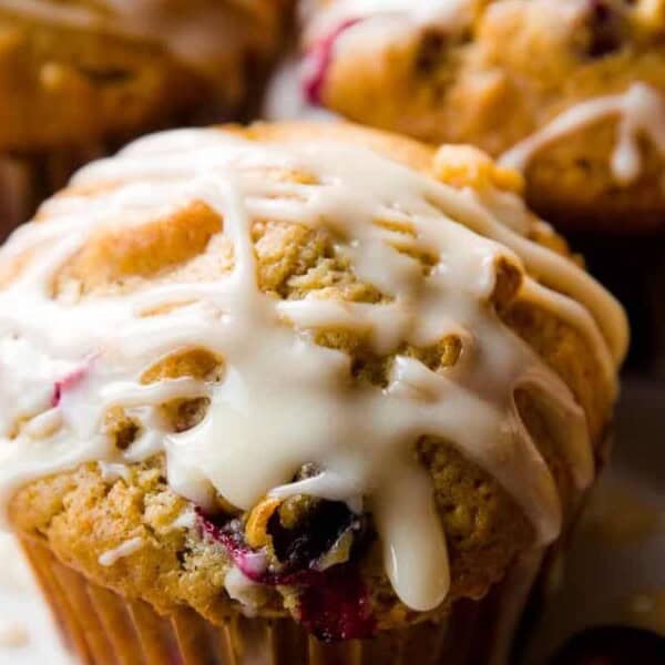 The image shows a close-up of a muffin with white icing on a white plate, surrounded by similar muffins.
