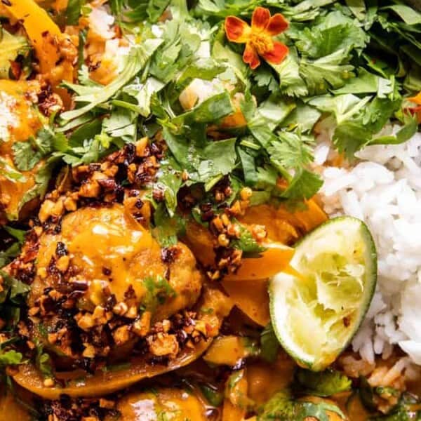 A bowl of rice topped with saucy meatballs, chopped cilantro, sliced lime, edible flowers, and crunchy chili bits.