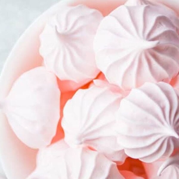 A bowl filled with light pink meringue cookies, each with a delicate, swirled pattern. The meringues have a smooth texture and are set against a light background.