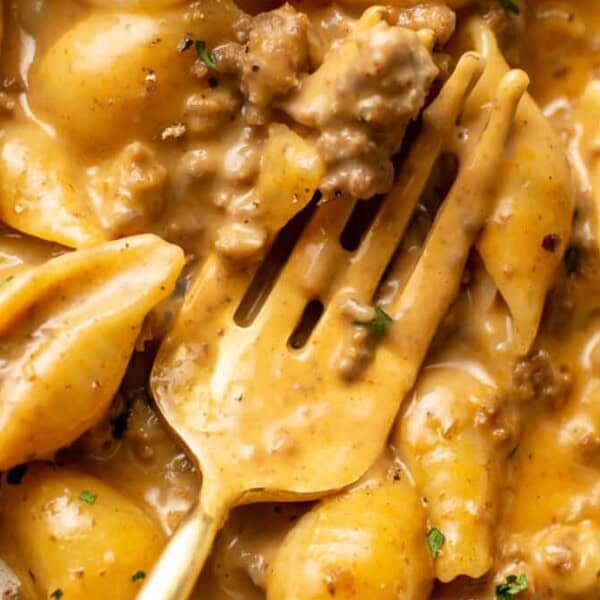 A close-up of creamy pasta shells mixed with ground beef in a rich, brownish-orange sauce, with a fork resting among the pasta.