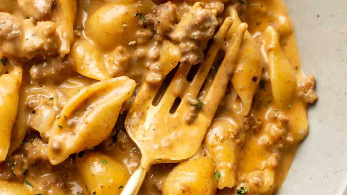 A close-up of creamy pasta shells mixed with ground beef in a rich, brownish-orange sauce, with a fork resting among the pasta.