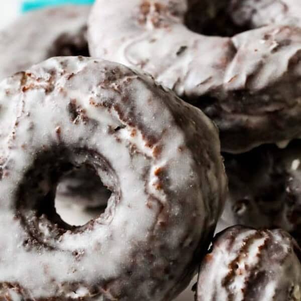 A plate of glazed chocolate cake donuts stacked closely together, with a teal cloth in the background.