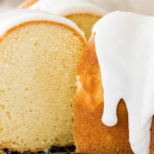 A Bundt cake with white icing is sliced, showing its moist, dense interior as it rests on a cooling rack.
