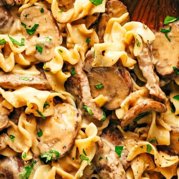 Close-up of beef stroganoff with egg noodles, mushrooms, and creamy sauce, topped with chopped parsley.