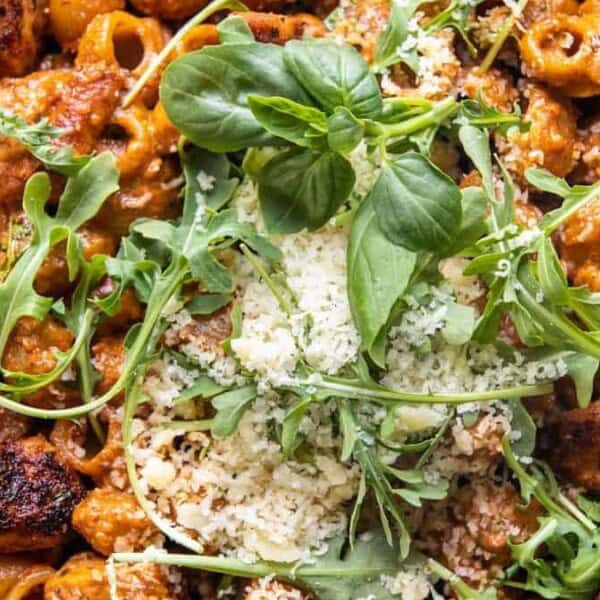 Close-up of pasta topped with grilled chicken, creamy tomato sauce, grated cheese, arugula, and spinach leaves.