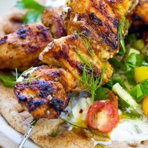 Grilled chicken skewers on a pita, topped with lettuce, tomatoes, and sauce.