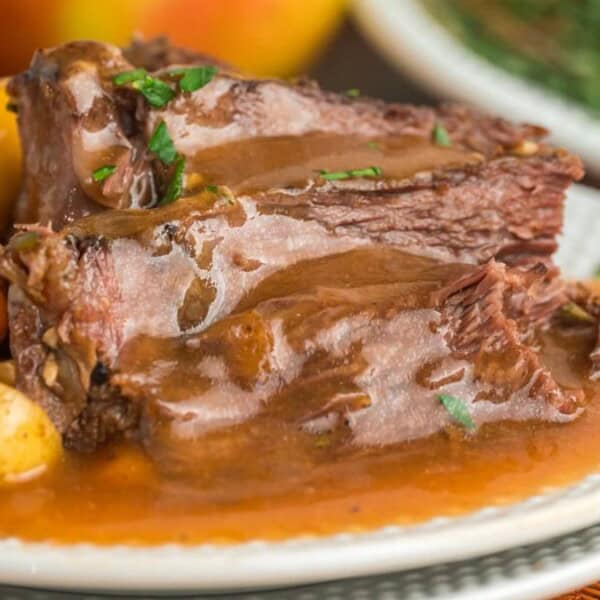 Pot roast with brown gravy, baby carrots, and potatoes served on a white plate.