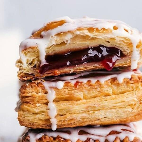 Two stacked flaky pastries with red fruit jam and white icing, surrounded by fresh strawberries.