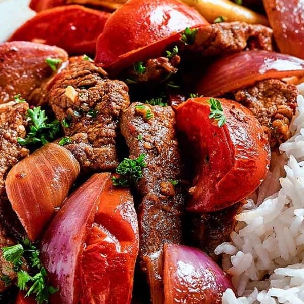 A plate with white rice, beef stir-fry, tomatoes, red onions, and fresh herbs.