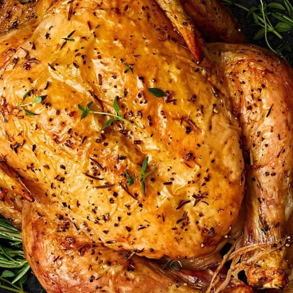 A whole roasted chicken with golden, crispy skin in a cast iron pan, garnished with fresh rosemary and thyme.
