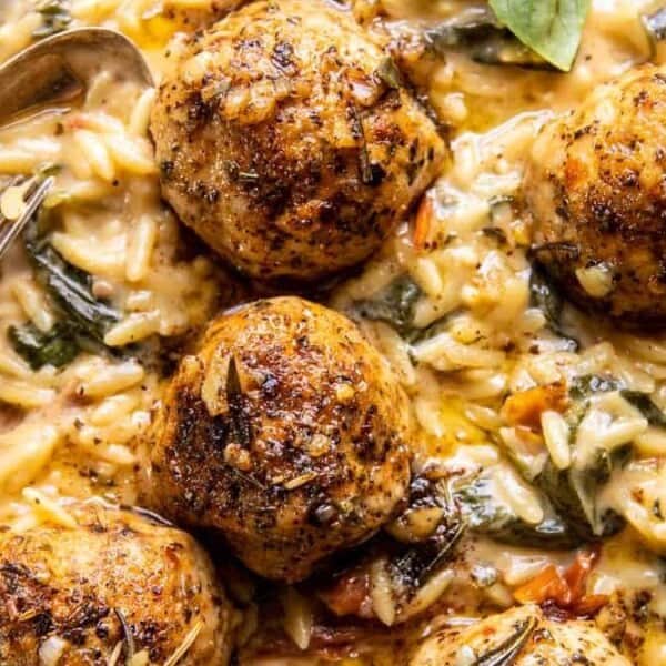 A plate of meatballs on creamy orzo pasta with spinach and fresh basil, served with a spoon.