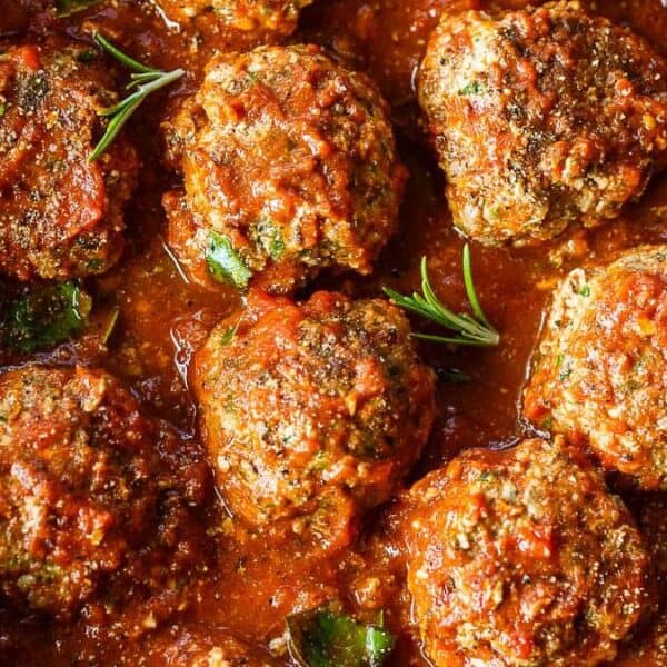 Meatballs simmering in tomato sauce, garnished with fresh rosemary sprigs.