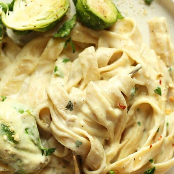 A plate of fettuccine alfredo topped with creamy sauce, halved Brussels sprouts, and chopped herbs.