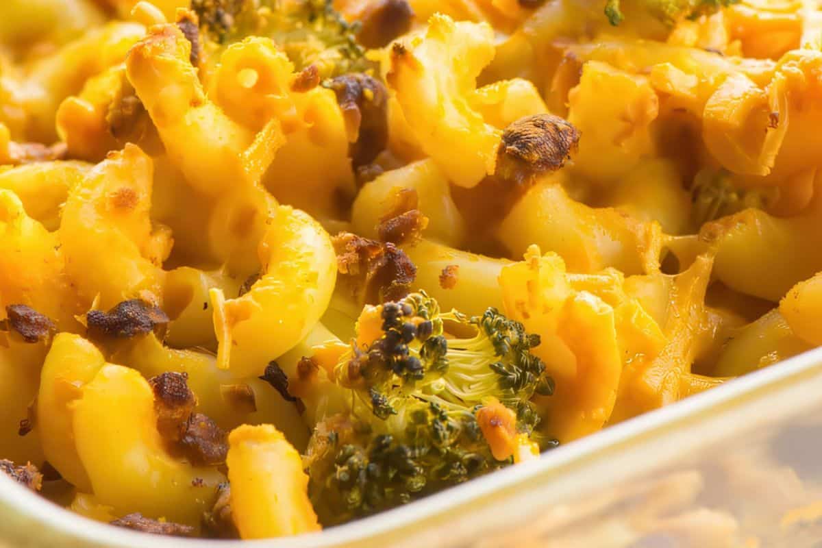A glass dish filled with baked macaroni and cheese, mixed with pieces of broccoli, topped with a browned, crispy cheese layer.