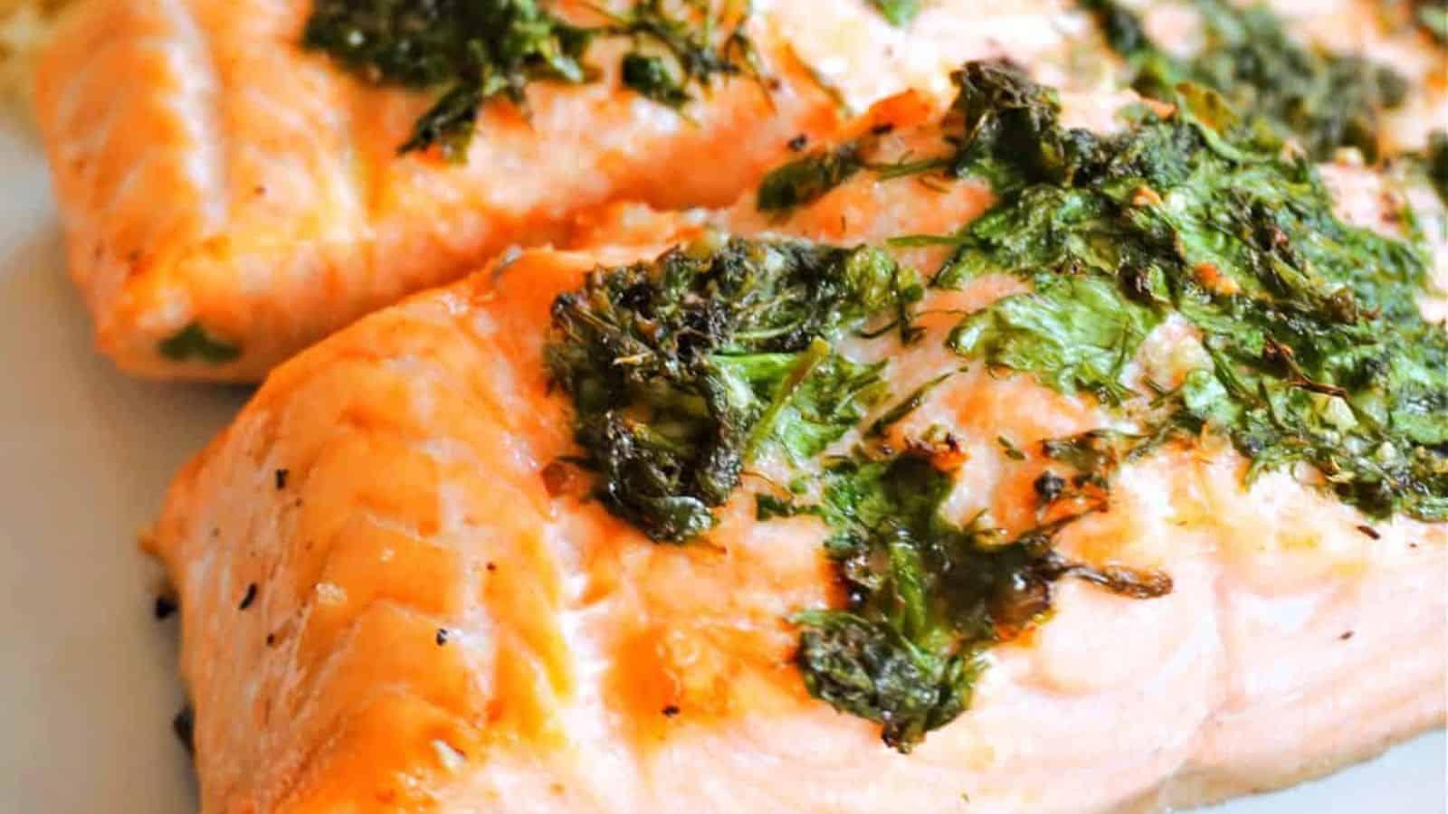 Close-up of cooked salmon fillets topped with chopped herbs on a white plate.