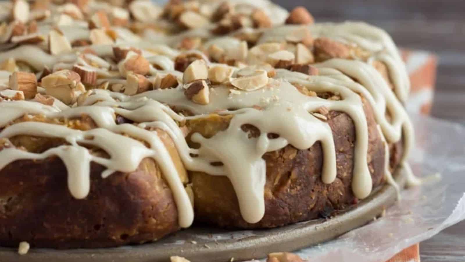 A round baked pastry with a glossy layer of white icing and sprinkled chopped nuts rests on parchment paper.
