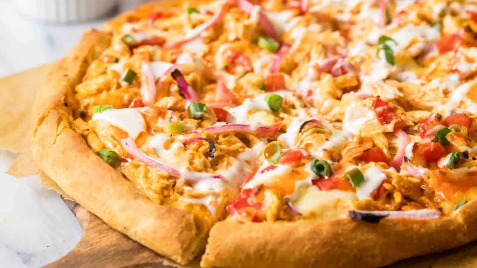 A thick-crust pizza topped with melted cheese, diced tomatoes, sliced green onions, red onions, and a drizzle of white sauce.