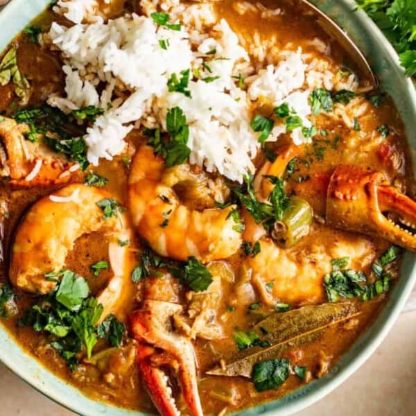 A bowl filled with rice, shrimp, crab claws, chopped vegetables, and herbs in a thick brown broth.