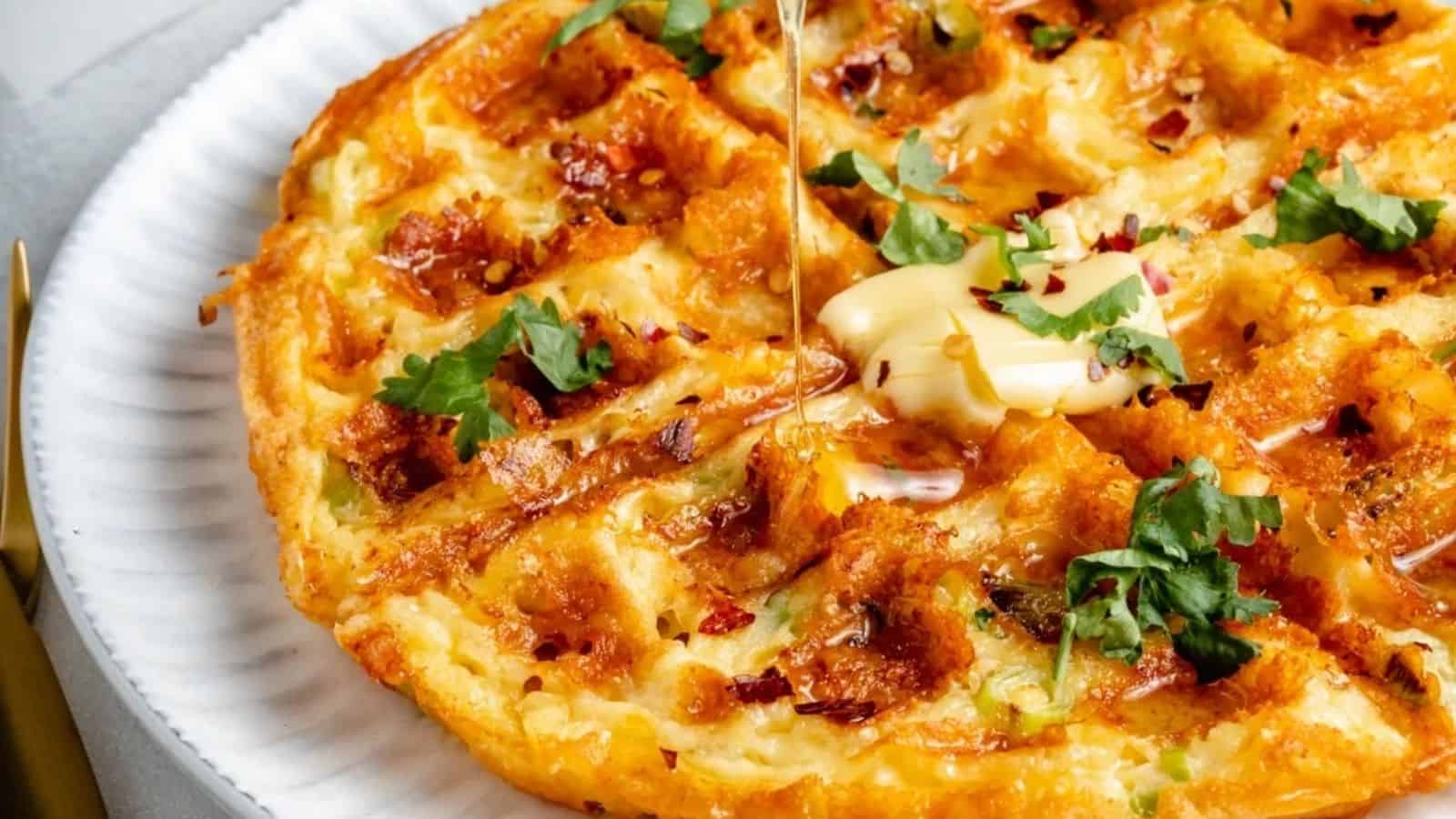 A waffle topped with a pat of butter, chopped fresh herbs, and syrup sits on a white plate.