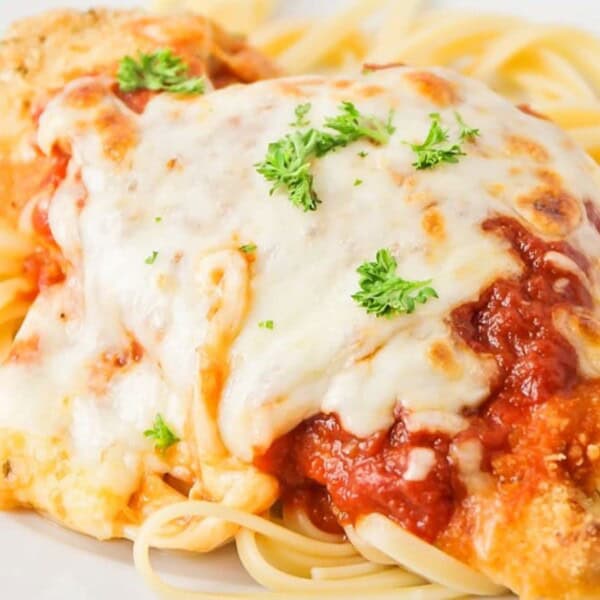 A plate with breaded chicken covered in melted cheese and tomato sauce, placed on pasta and sprinkled with chopped parsley.