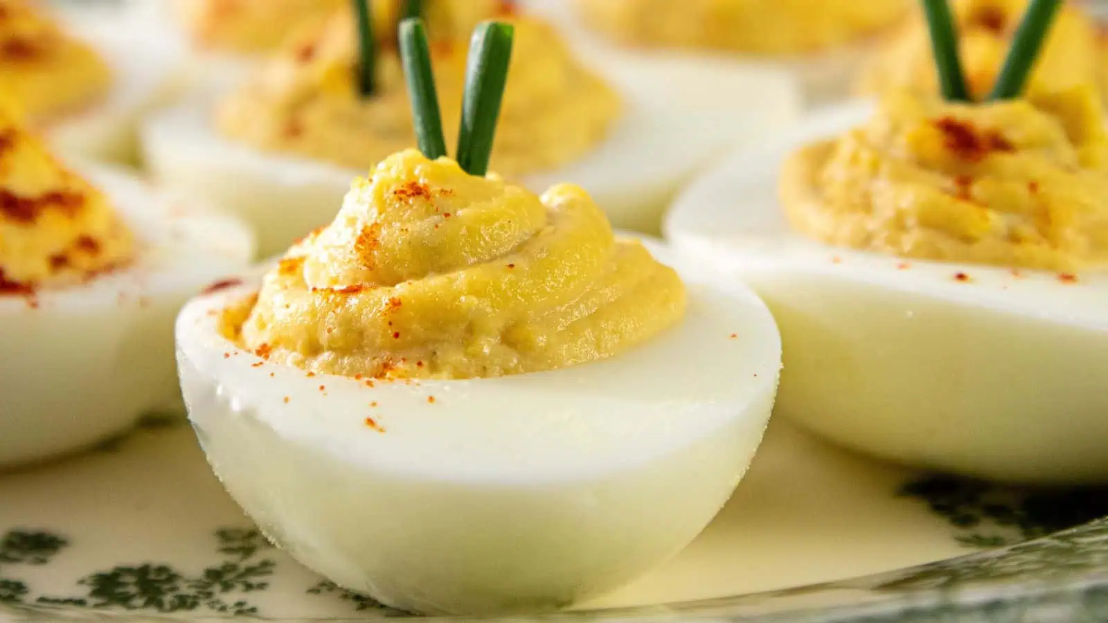 Close-up of Southern deviled eggs on a plate, filled with a creamy yellow yolk mixture and sweet pickle relish, garnished with green chives and a sprinkle of paprika. The eggs are neatly arranged and appear ready to serve.