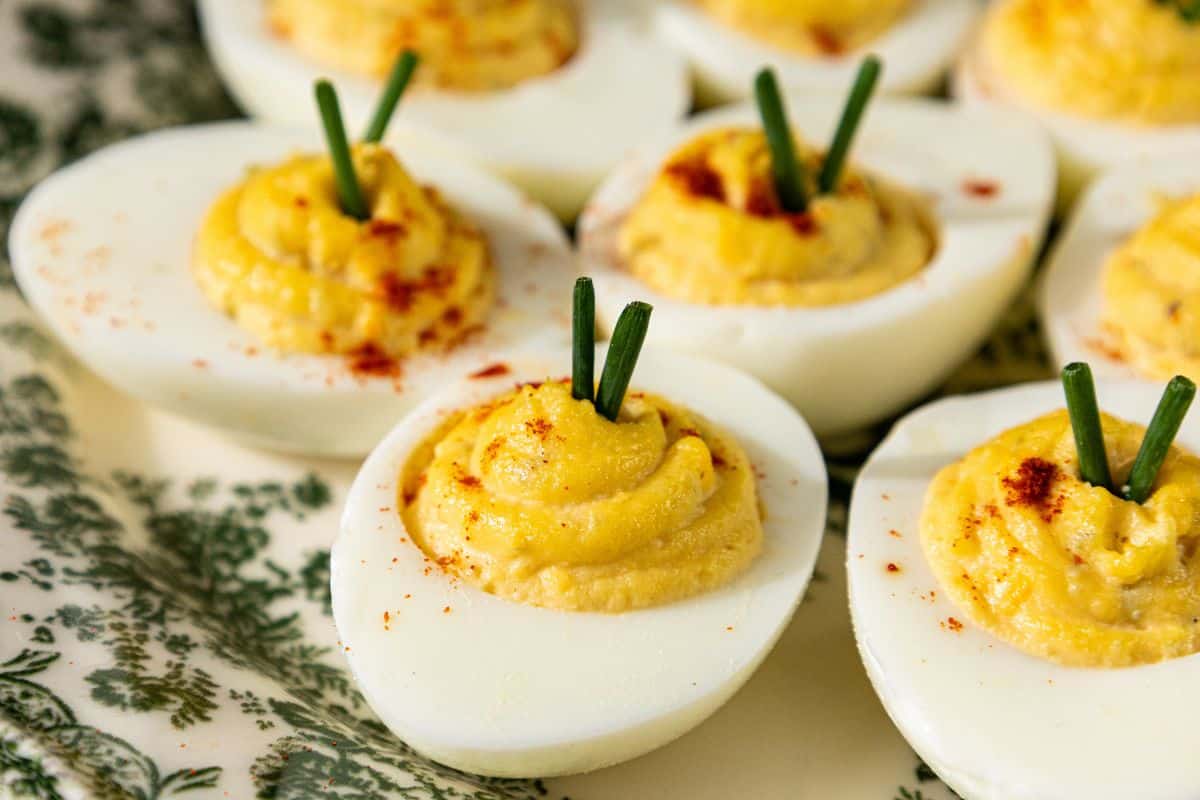 Deviled eggs topped with paprika and chopped chives, arranged on a decorative plate.