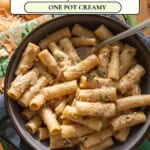 A bowl of rigatoni pasta with a creamy sauce and caramelized onions, garnished with herbs, sits on a wooden table. Above the bowl is text that reads: "French Onion Rigatoni - One Pot Creamy.