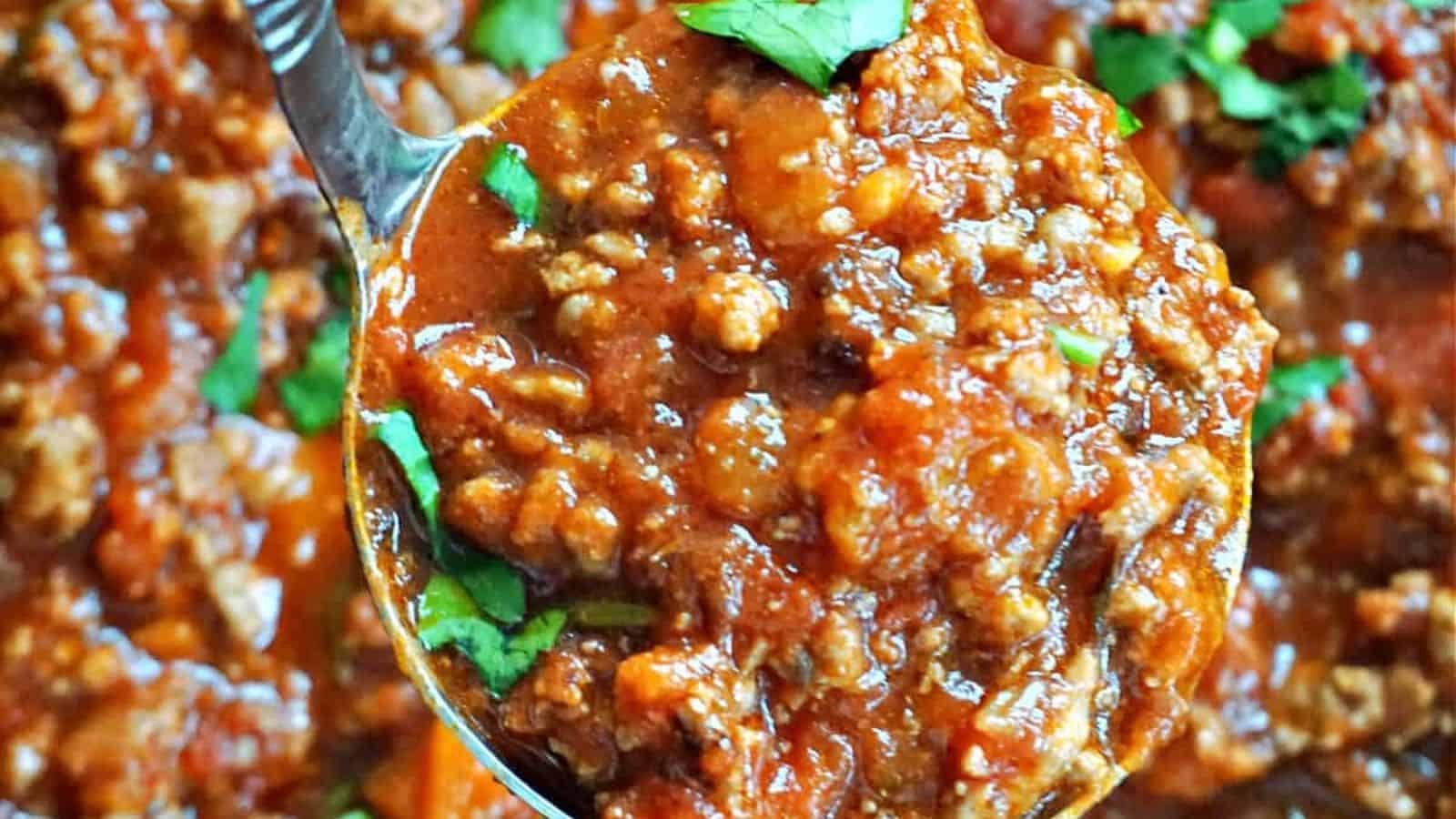 A spoon holding a chunky, tomato-based meat sauce topped with chopped parsley.