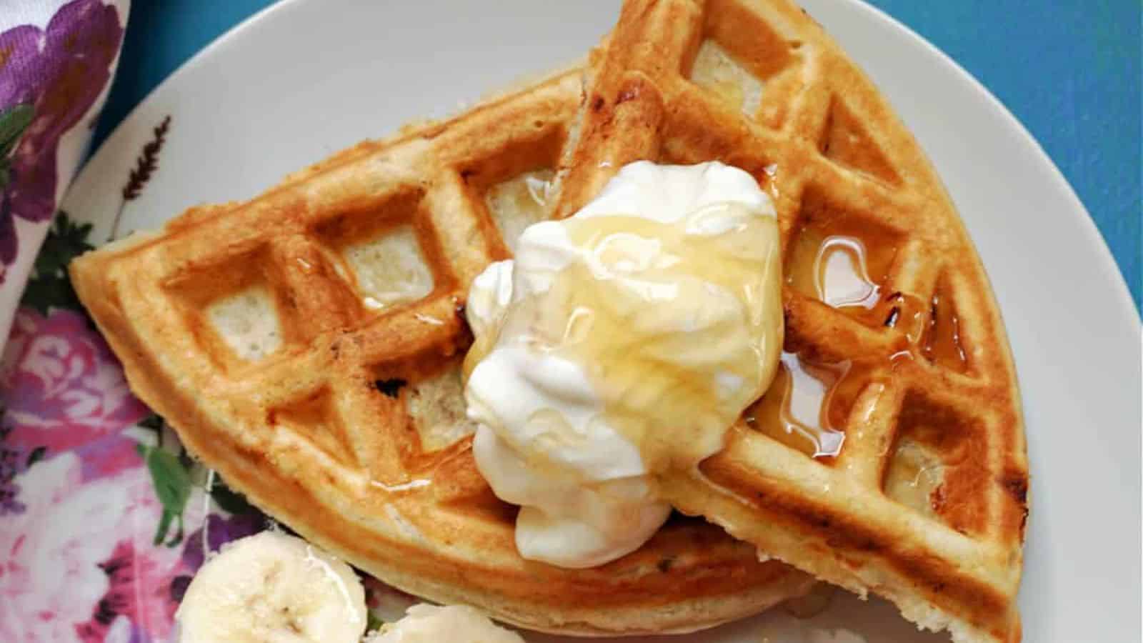 A plate with two waffle quarters topped with whipped cream and honey, served with banana slices on the side.