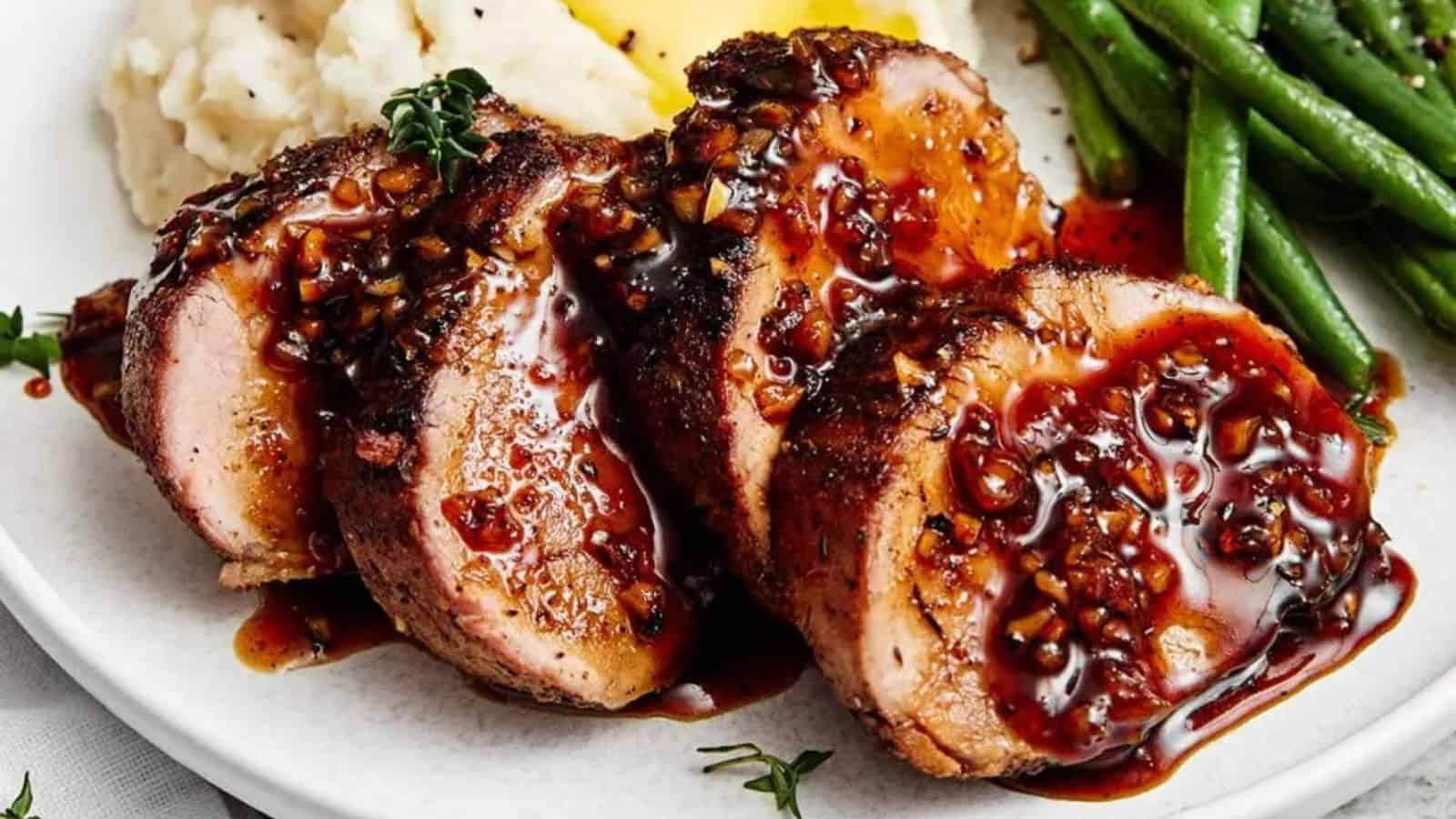 Three slices of pork tenderloin with a dark glaze, mashed potatoes, and green beans on a white plate.